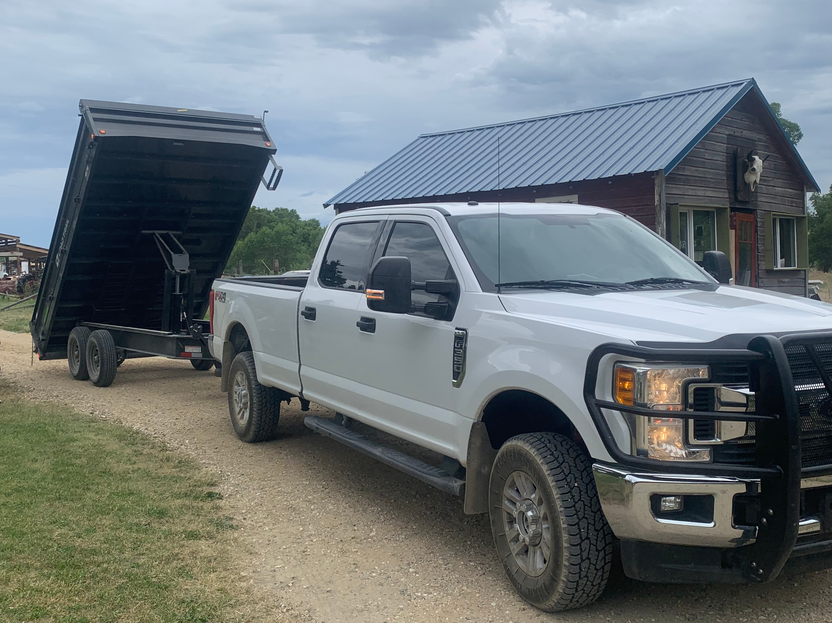 A white one ton truck and black drop trailer fully extented into the air.